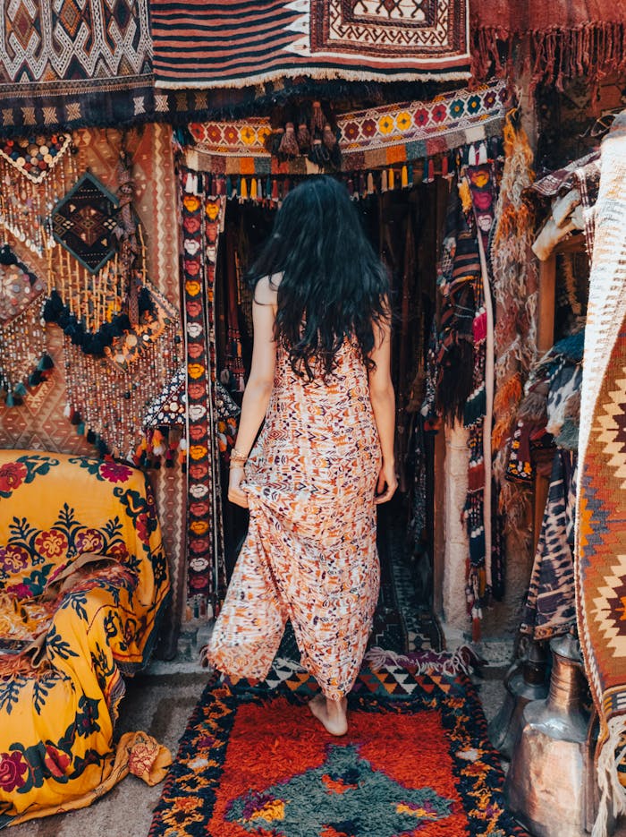 A woman in a flowing dress explores a colorful traditional market filled with textiles and intricate patterns.
