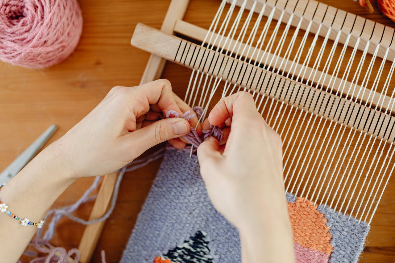 Detailed close-up of hands weaving colorful yarn on a wooden loom, showcasing the art of handmade textile craft.