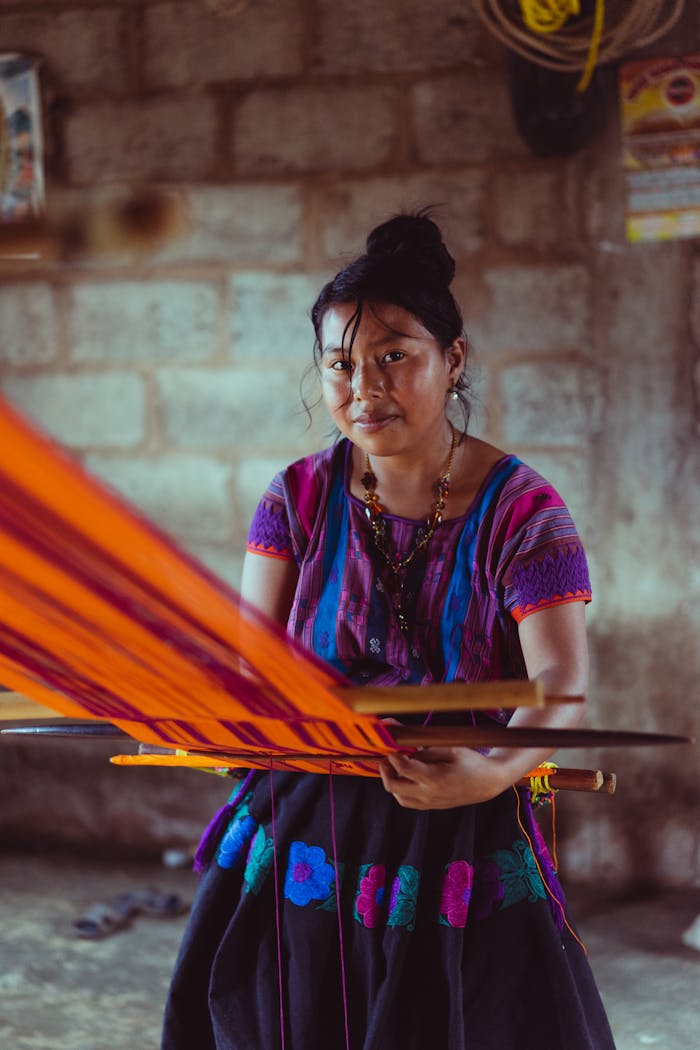 Indigenous Mexican woman weaving colorful fabric on a traditional loom inside a rustic setting.